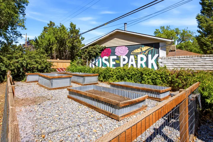 Gravel ground cover with multiple raised garden beds, wood fence with wire mesh, and mature perimeter trees