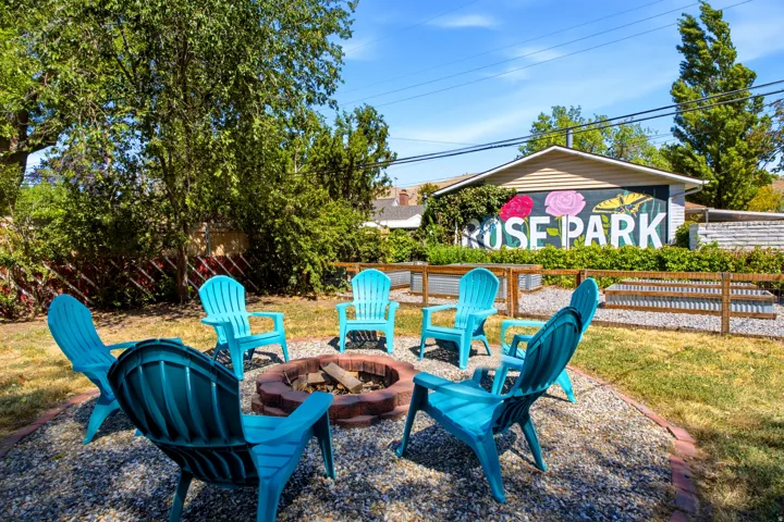 Gravel patio area featuring a built-in fire pit, surrounded by green landscaping and mature trees