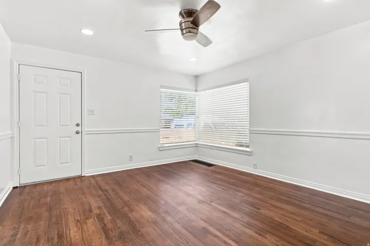 Hardwood flooring, white paneled door, recessed lighting, ceiling fan, and corner windows with blinds