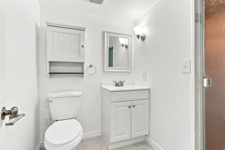 White vanity with a single basin sink, wall-mounted light fixture, framed mirror, and a glass-enclosed shower