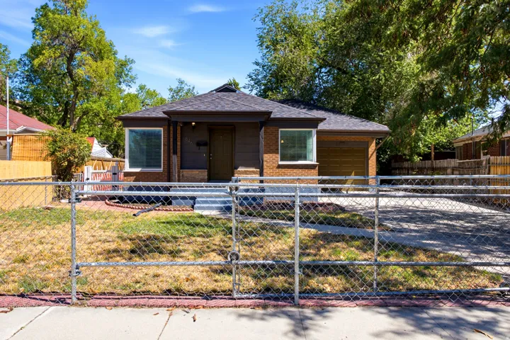 Brick and siding exterior with a dark shingle roof, featuring a chain-link fence, an integrated garage, and a paved driveway