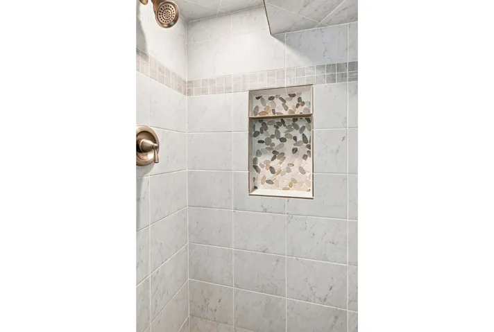 Subway tile shower with recessed niche with pebble tile, and a brushed nickel shower fixture