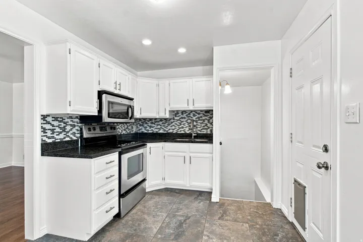 White cabinetry with stainless steel appliances, dark countertops, and mosaic tile backsplash