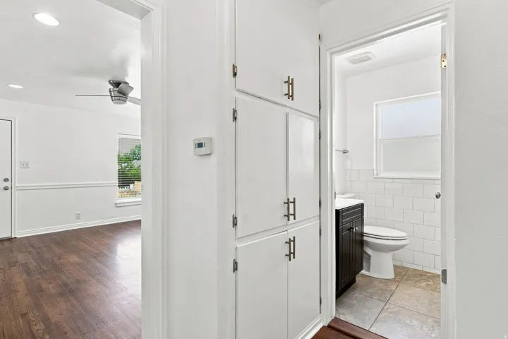 Built-in hallway storage with brushed nickel hardware, wood-finish flooring, ceiling fan, and a bathroom featuring subway tile and a dark wood-finish vanity