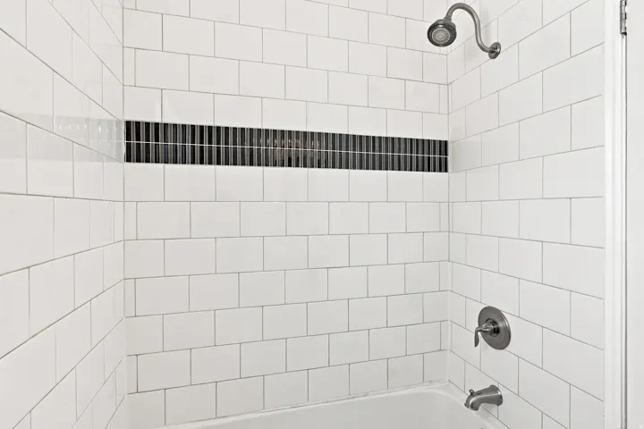 White subway tile surround with a dark tile accent band, brushed nickel showerhead and faucet, and white bathtub