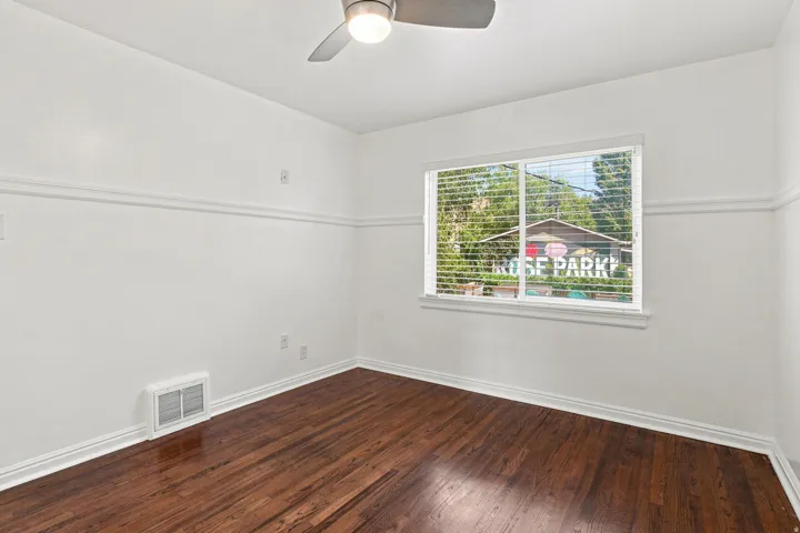 Hardwood-finish flooring, crisp white walls with chair rail molding, ceiling fan with integrated lighting, and a window featuring blinds