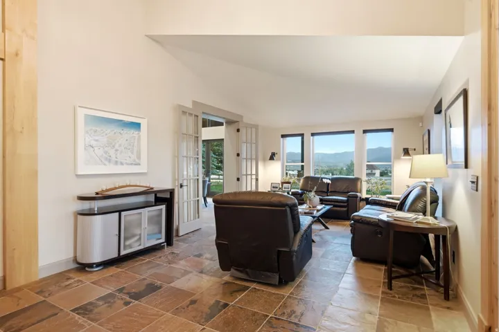 Vaulted ceiling, French doors, large windows, wall sconces, and stone tile flooring
