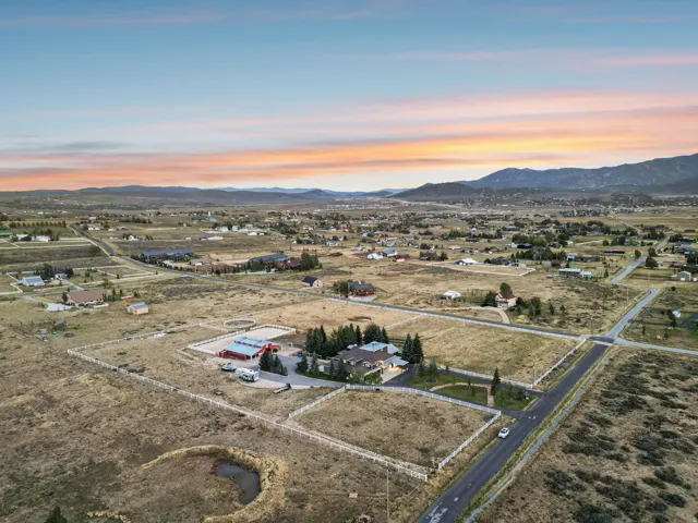 Expansive property featuring a main residence, an additional structure with a red roof, fenced pastures, and a circular riding arena