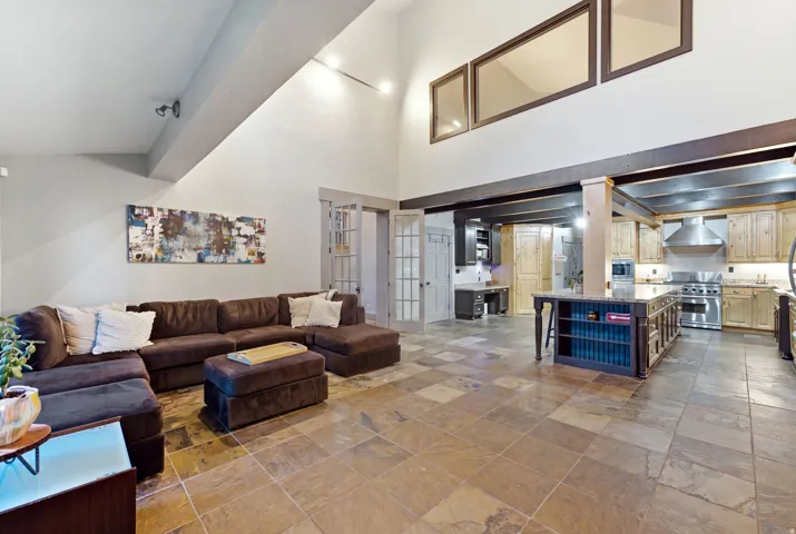 Vaulted ceilings with exposed beams, natural stone tile flooring, kitchen island with built-in shelving, stainless steel appliances, and wood cabinetry