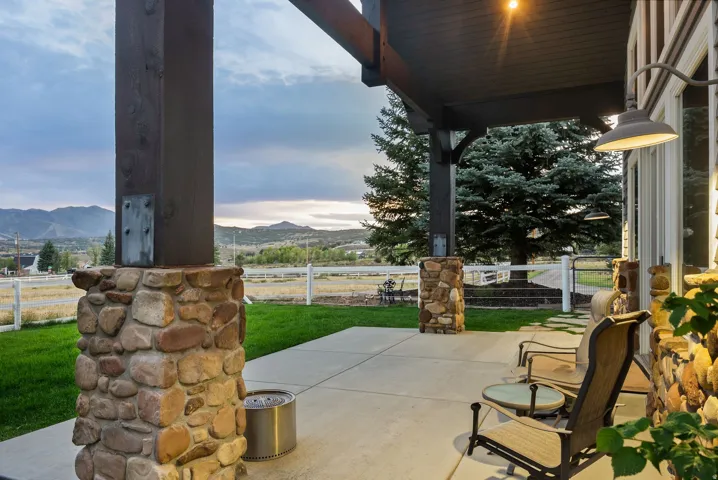 Expansive concrete patio featuring stone-clad pillars, wood-beam overhang, and exterior wall lighting