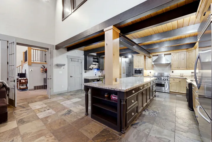 Gourmet kitchen featuring a large central island, stainless steel appliances, wood beam ceiling, and stone tile flooring