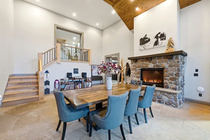 Vaulted wood-paneled ceiling, stone fireplace with hearth, flagstone flooring, wood staircase with metal balusters, and recessed lighting