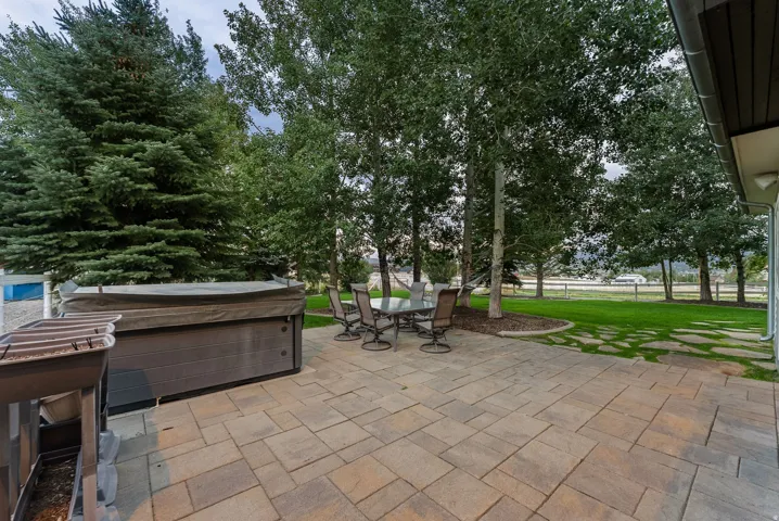 Paved patio with a hot tub, surrounded by mature trees and a manicured lawn