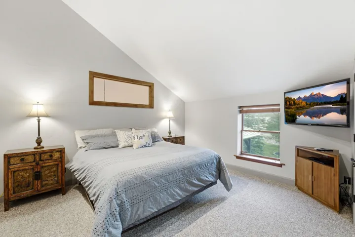 Sloped ceiling room featuring a window with wood trim, light gray walls, and light-colored carpet flooring