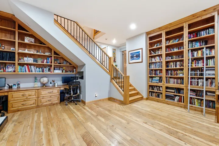 Wood-finish flooring, built-in shelving, built-in desk, wood staircase with metal railing, recessed lighting