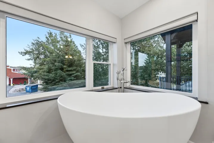 Freestanding soaking tub with floor-mounted faucet, corner windows, and roller shades