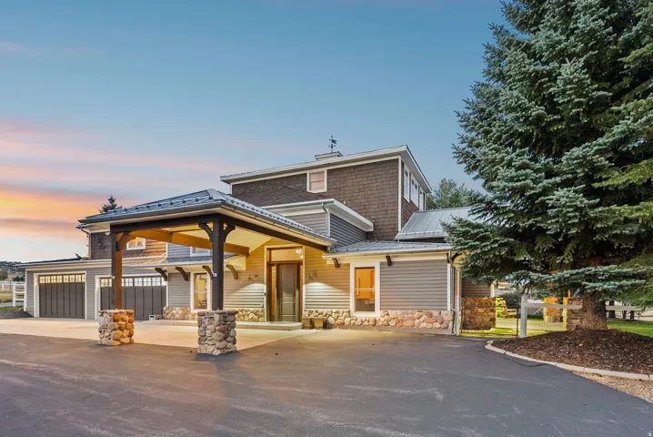 Custom porte-cochère entrance with stone pillars, multi-level exterior siding, two-car garage with dark wood-finish doors, and mature evergreen landscaping