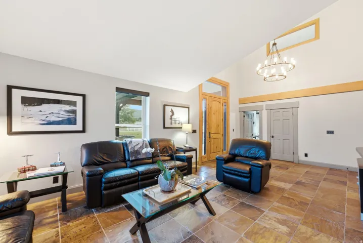 Vaulted ceiling with an ornate chandelier, transom windows, natural wood-finish door, and large-format tile flooring