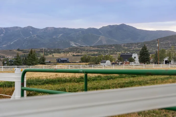 Expansive property with a white perimeter fence, verdant fields, and distant mountain backdrops