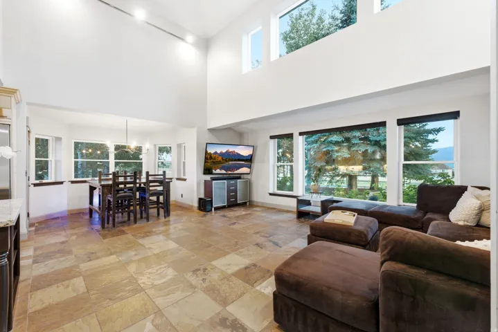 Vaulted ceilings, large format tile flooring, a dining area with a chandelier, and expansive windows