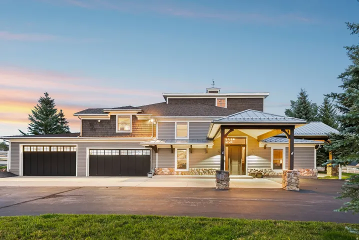 Exterior featuring stone accents, multi-pane garage doors, covered entry with timber framing, and a metal roof over the entry