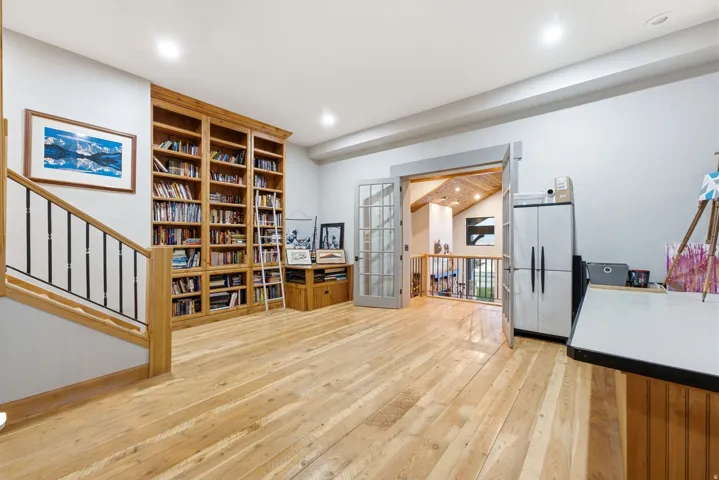 Hardwood flooring, custom built-in wood shelving, wood banister with metal balusters, recessed lighting, and French doors