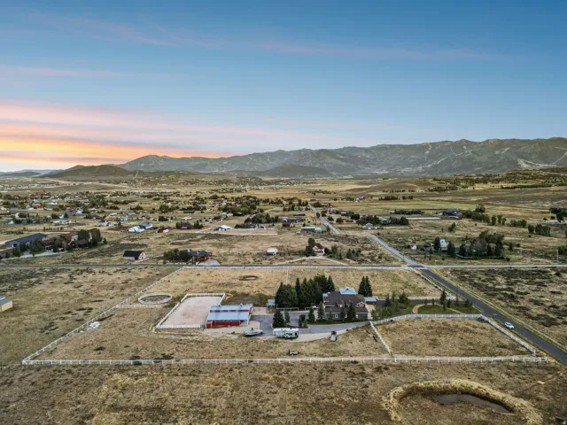 Expansive grounds featuring a main residence, a red barn structure, white perimeter fencing, and a distinct equestrian ring