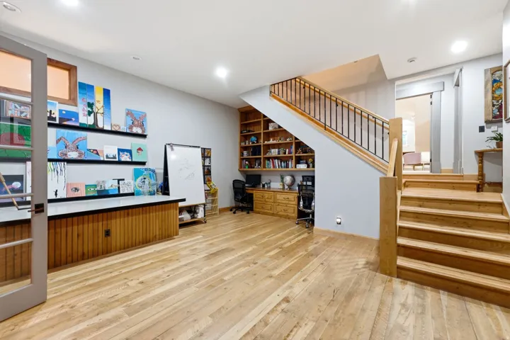 Hardwood flooring, built-in shelving, wood staircase with iron balusters, recessed lighting, and a built-in wood cabinet