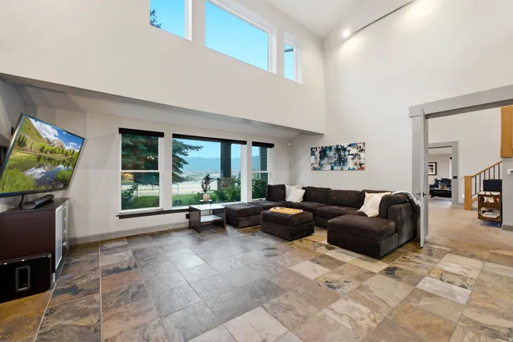 Spacious living area featuring high ceilings, slate tile flooring, and abundant natural light from large windows