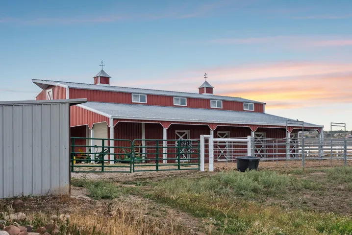 Red barn structure featuring a metal roof, multiple cupolas with weathervanes, and white trim accents