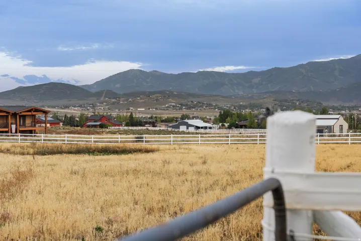 Expansive field with a white rail fence, distant mountain range, and scattered residential structures