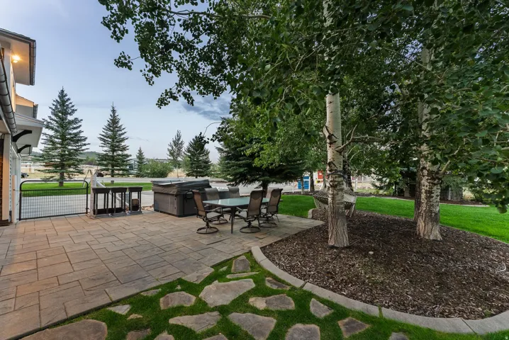 Expansive paver patio with a stone path, lush lawn, and mature trees