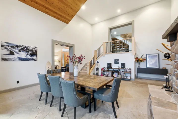 Vaulted ceilings with wood paneling, natural stone flooring, stone fireplace, light wood staircase with black metal balusters, and recessed lighting