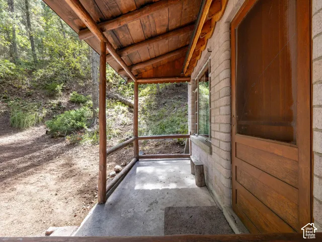 Covered porch featuring a concrete floor, wood-finish railing, and exposed wood ceiling