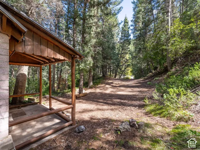 Covered porch with log railings and a concrete floor, surrounded by a natural wooded landscape