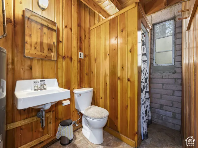 Wood paneling throughout, white wall-mounted basin sink with a chrome faucet, white toilet, and a window with a brick surround