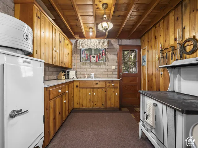 Wood paneling throughout, exposed wood beam ceiling, brick accent wall, wood cabinetry with white hardware, and a wood-panel exterior door