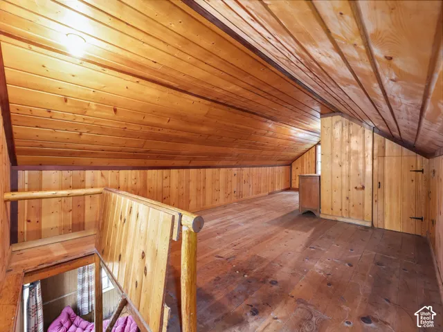 Sloped ceiling with wood-paneled finish, wood-plank flooring, and built-in storage cabinet