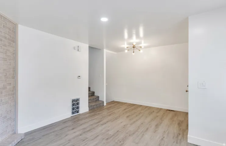 Light wood-finish flooring, white walls, modern ceiling light fixture, and brick-textured accent wall