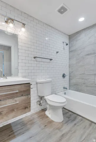 Floating wood-finish vanity with an integrated sink, subway tile wall, large format tile shower surround, and a white bathtub