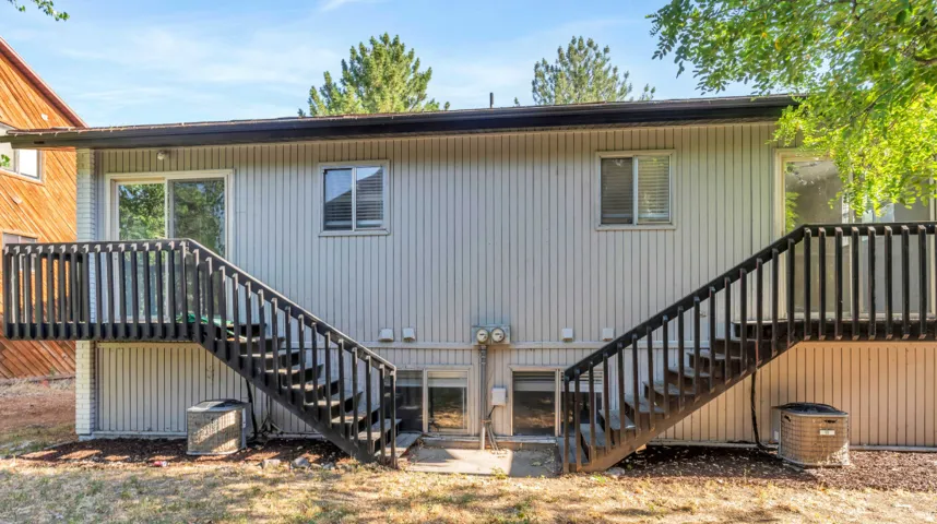 Rear exterior featuring light-colored vertical siding, two dark-stained wood decks with railings, sliding glass doors, and two ground-level windows