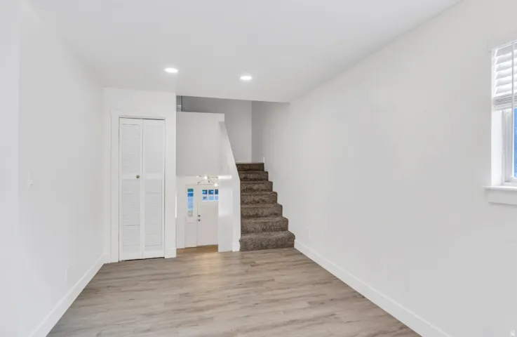 Recessed lighting, wood-finish flooring, white walls, louvered bi-fold doors, and a window with blinds