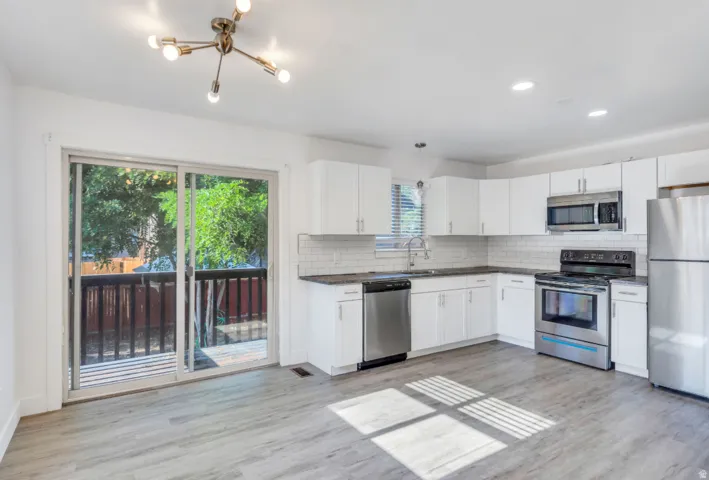 Open-concept kitchen with white shaker cabinetry, stainless steel appliances, and wood-finish flooring