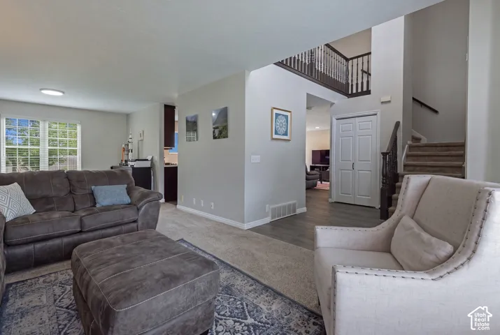 Carpeted living area with a large window, light gray walls, wood-finish flooring, and a visible staircase with dark wood railings