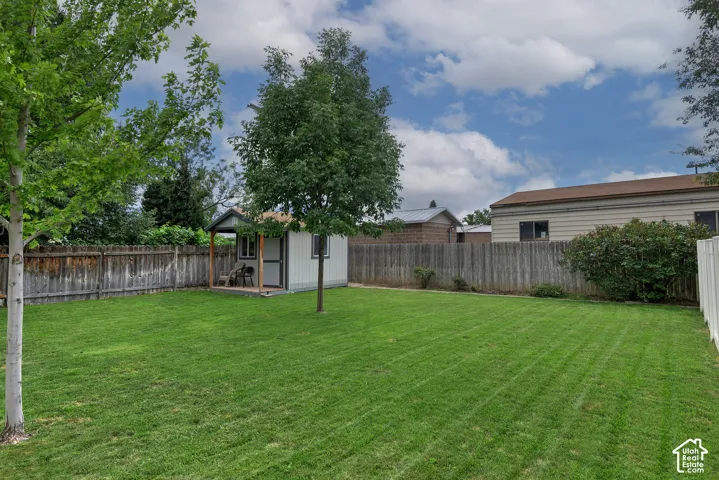 Expansive backyard featuring a manicured lawn, wood privacy fencing, mature trees, and an outbuilding with a covered porch