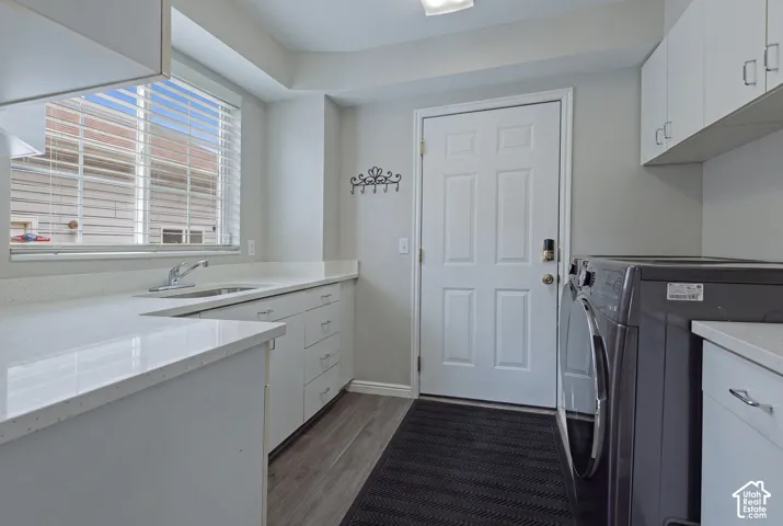 Laundry area featuring abundant white cabinetry, light-toned countertops, a stainless steel sink, and wood-finish flooring