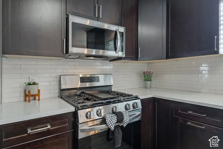 Dark wood-finish cabinetry with brushed nickel hardware, stainless steel gas range, stainless steel microwave, white subway tile backsplash, and light-toned countertops