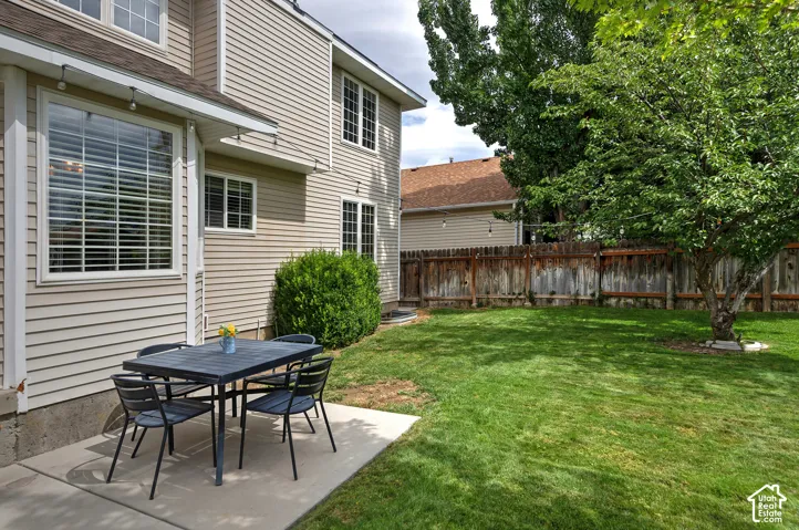 Siding exterior with multiple windows, concrete patio, and a manicured lawn with mature trees