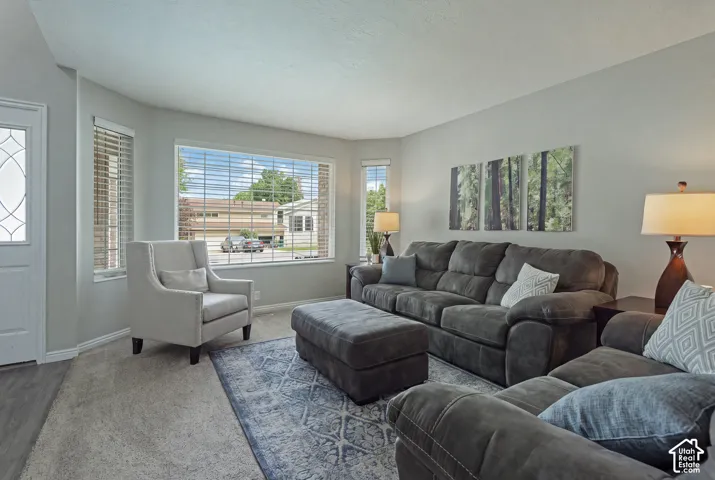 Recessed lighting illuminates a spacious living area featuring a large bay window, carpeted flooring, and light gray wall finishes