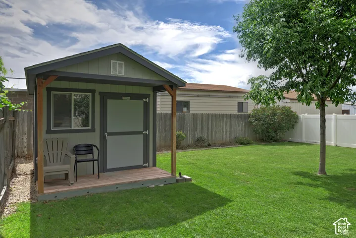 Expansive grassy yard featuring a storage shed with a covered porch and a mature tree